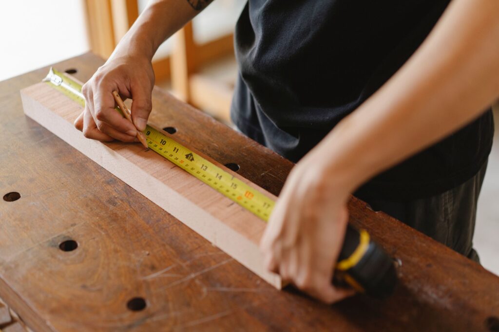 Hands marking a board with a pencil and a tape measure