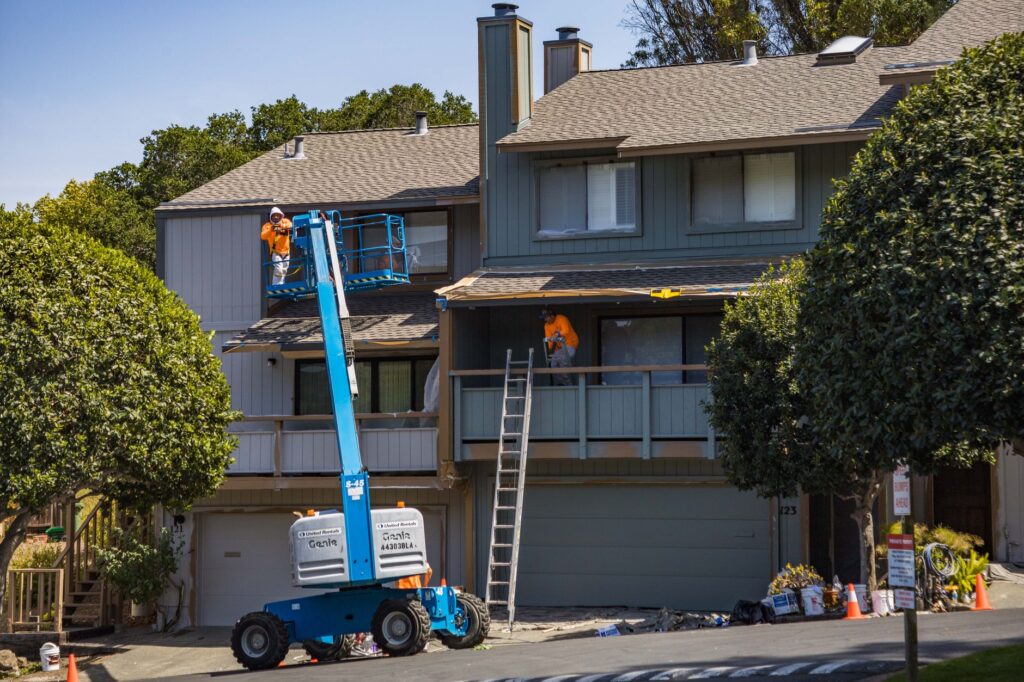 A lift and ladders beside a townhouse during exterior work