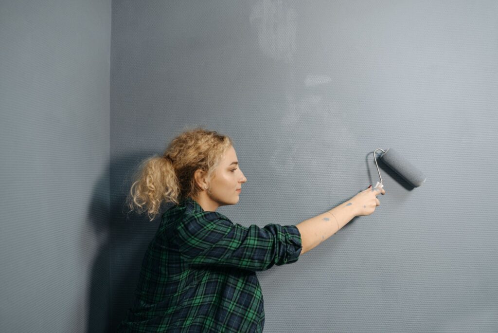 A painter rolling a fresh gray coat onto a wall